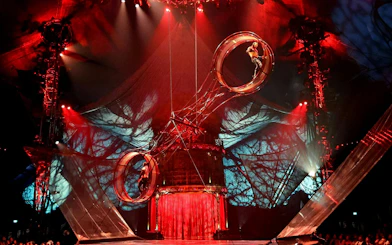 Performer on rotating wheel during Kooza stage show with dramatic lighting.