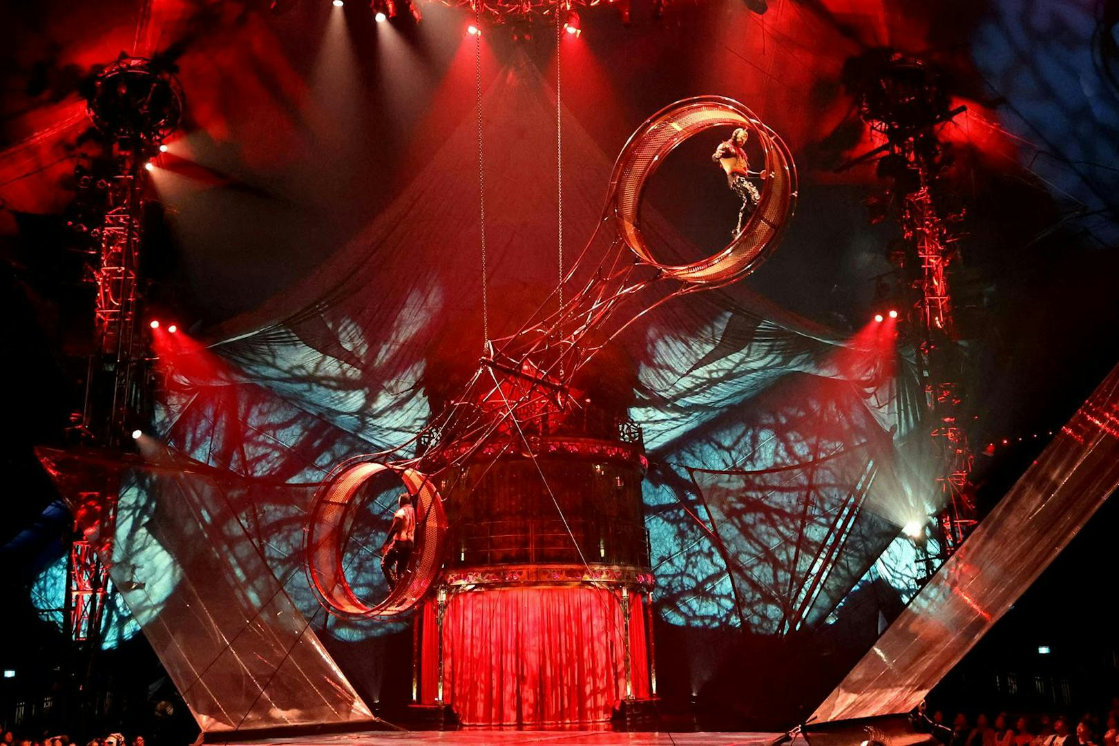 Performer on rotating wheel during Kooza stage show with dramatic lighting.