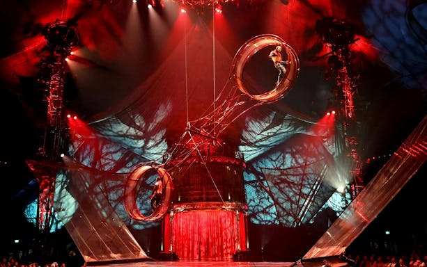 Performer on rotating wheel during Kooza stage show with dramatic lighting.
