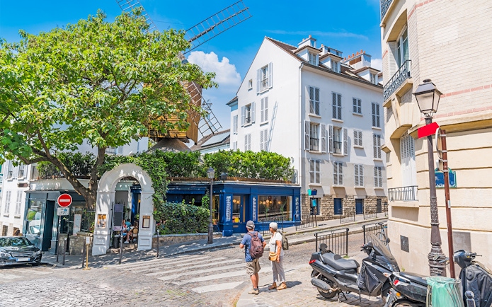 Street view of Montmartre, Paris with a historic windmill and tourists exploring.