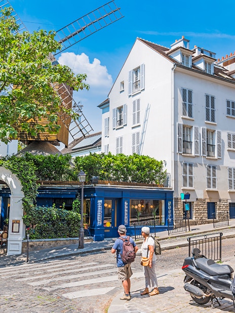 Street view of Montmartre, Paris with a historic windmill and tourists exploring.