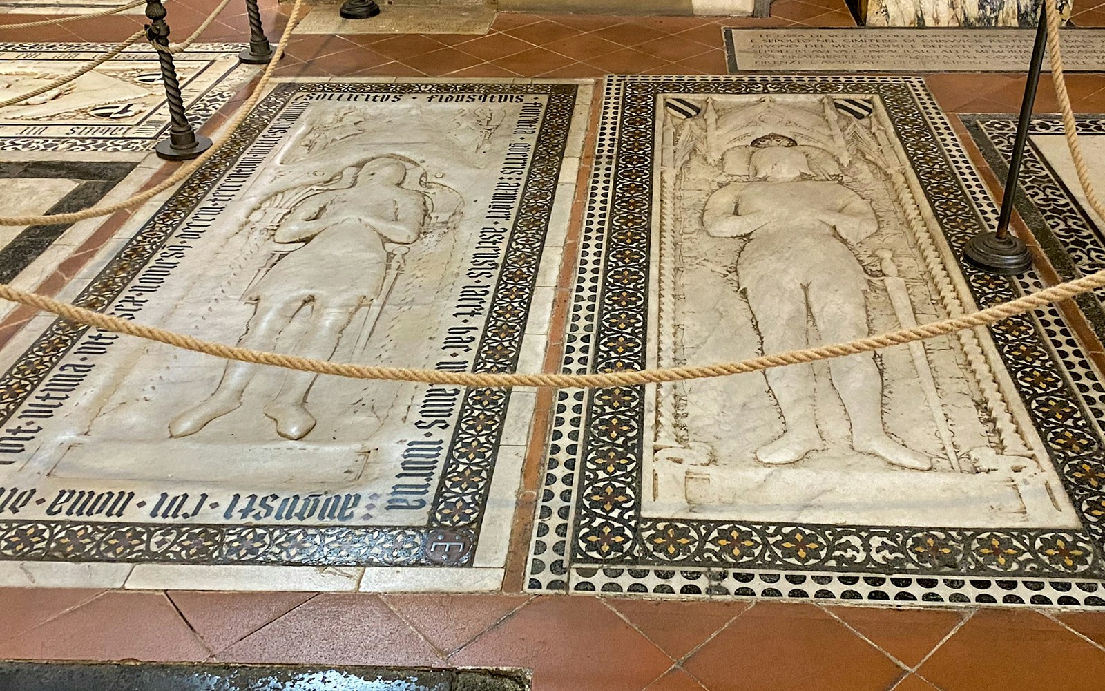 Tombstones inside Santa Croce, Florence, featuring detailed carvings and inscriptions.