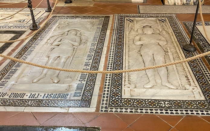 Tombstones inside Santa Croce, Florence, featuring detailed carvings and inscriptions.
