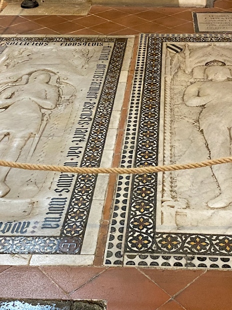 Tombstones inside Santa Croce, Florence, featuring detailed carvings and inscriptions.