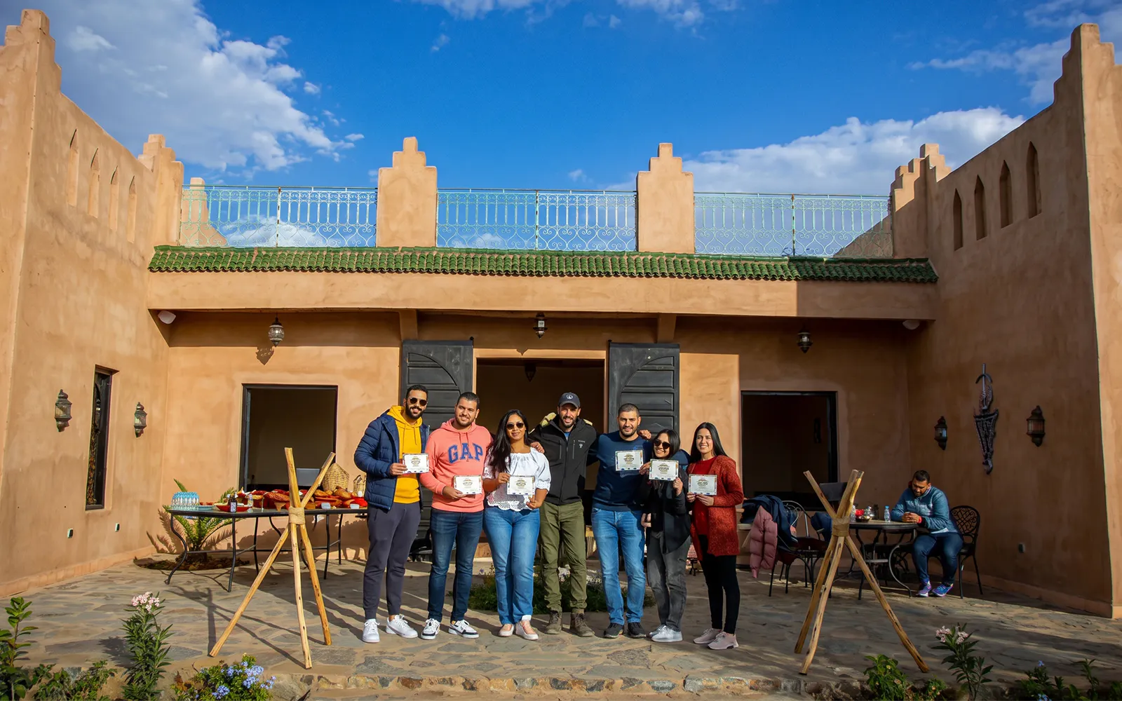 Group holding certificates outside a traditional Marrakesh building after a sunrise hot air balloon flight.