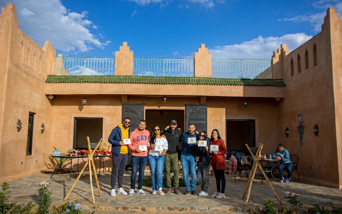 Group holding certificates outside a traditional Marrakesh building after a sunrise hot air balloon flight.
