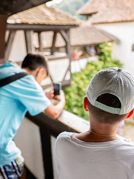 Boy looking into Bran Castle courtyard, capturing the view with a smartphone.
