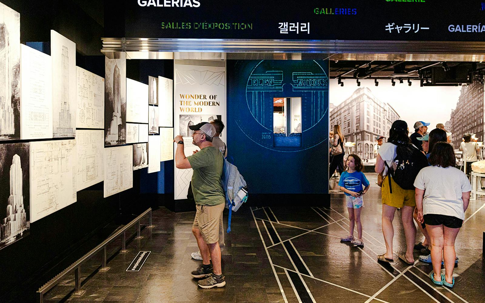 Visitors exploring Empire State Building exhibit with architectural drawings.