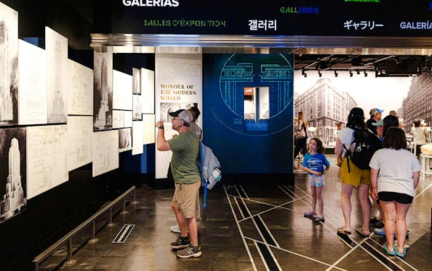 Visitors exploring Empire State Building exhibit with architectural drawings.