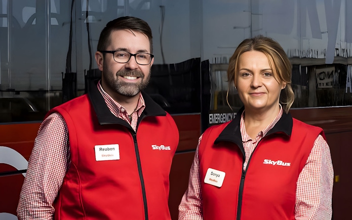 Skybus staff in red vests standing in front of Melbourne Airport shuttle bus.