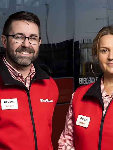 Skybus staff in red vests standing in front of Melbourne Airport shuttle bus.