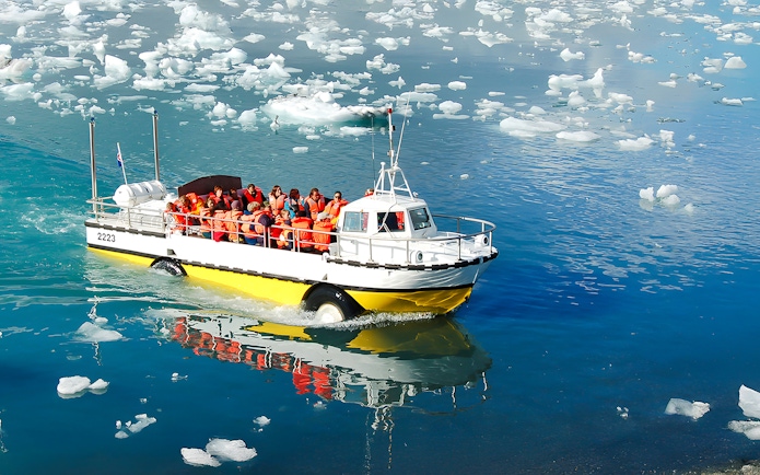 Boat with tourists on Jökulsárlón Glacial Lagoon, Iceland, surrounded by icebergs.