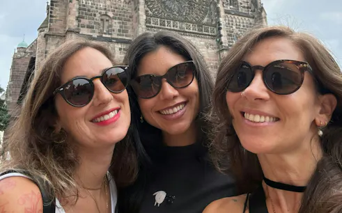 Three people smiling in front of a medieval church in Nuremberg during a self-guided city exploration game.