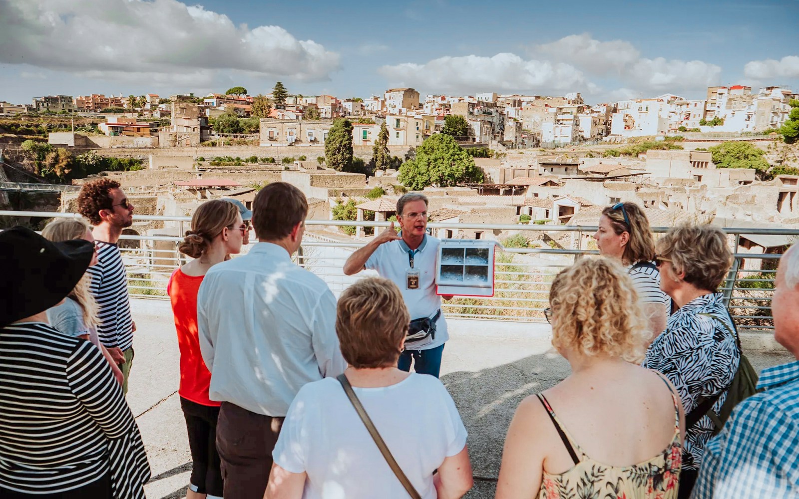 Group listening to a guide at Herculaneum with city ruins in the background.