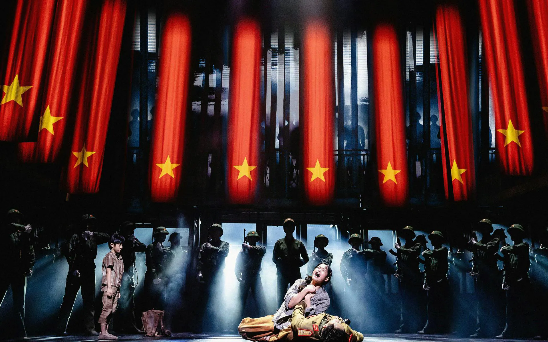 Miss Saigon performance with actors on stage, West End, red flags in background.