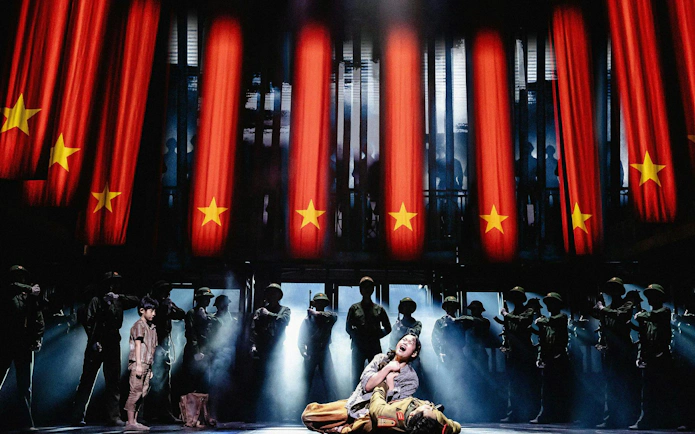 Miss Saigon performance with actors on stage, West End, red flags in background.