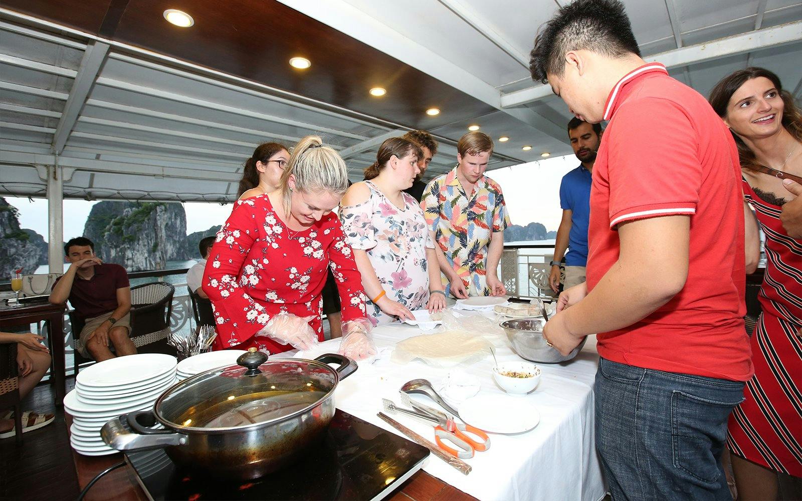 Cooking class on Halong Bay cruise with tourists preparing dishes.