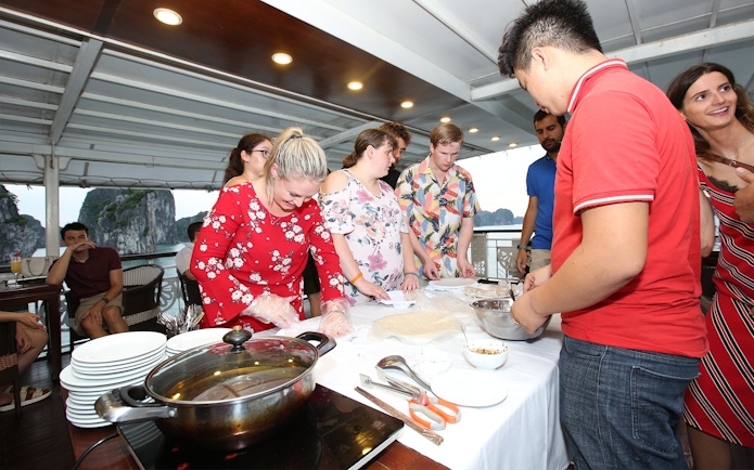 Cooking class on Halong Bay cruise with tourists preparing dishes.