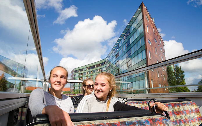 Tourists enjoying a hop-on hop-off bus tour in Tallinn with modern architecture in the background.