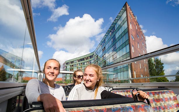 Tourists enjoying a hop-on hop-off bus tour in Tallinn with modern architecture in the background.