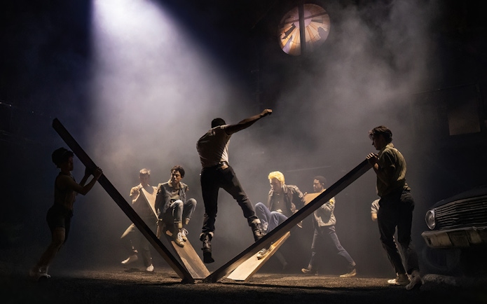 Stage performance of "The Outsiders" with actors on a dramatic set.
