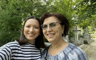 Two people smiling in Bellu Cemetery, Bucharest, surrounded by gravestones and greenery.