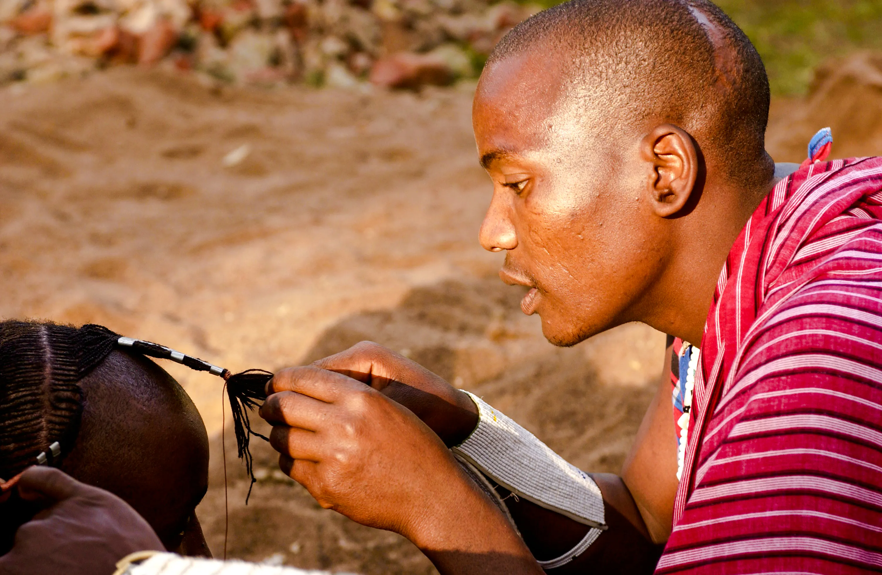 Maasai man braiding hair in a village, Zanzibar.