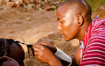 Maasai man braiding hair in a village, Zanzibar.