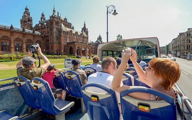 Tourists on an open-top bus in Glasgow photographing Kelvingrove Art Gallery.