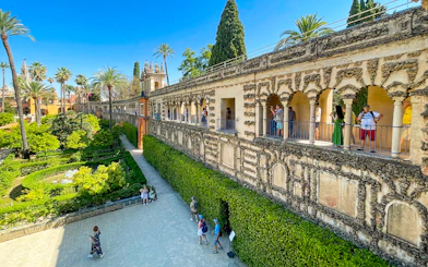 Alcazar of Seville garden view with tourists on a guided tour along the ornate stone gallery.