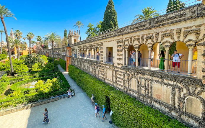 Alcazar of Seville garden view with tourists on a guided tour along the ornate stone gallery.