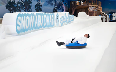 Person tubing down snowy slope at Snow Abu Dhabi indoor park.