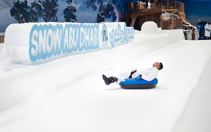 Person tubing down snowy slope at Snow Abu Dhabi indoor park.