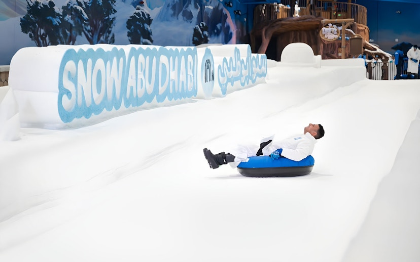 Person tubing down snowy slope at Snow Abu Dhabi indoor park.