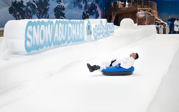 Person tubing down snowy slope at Snow Abu Dhabi indoor park.