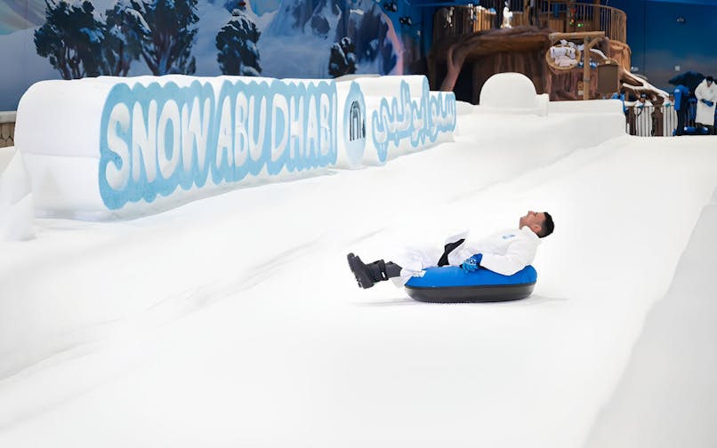 Person tubing down snowy slope at Snow Abu Dhabi indoor park.