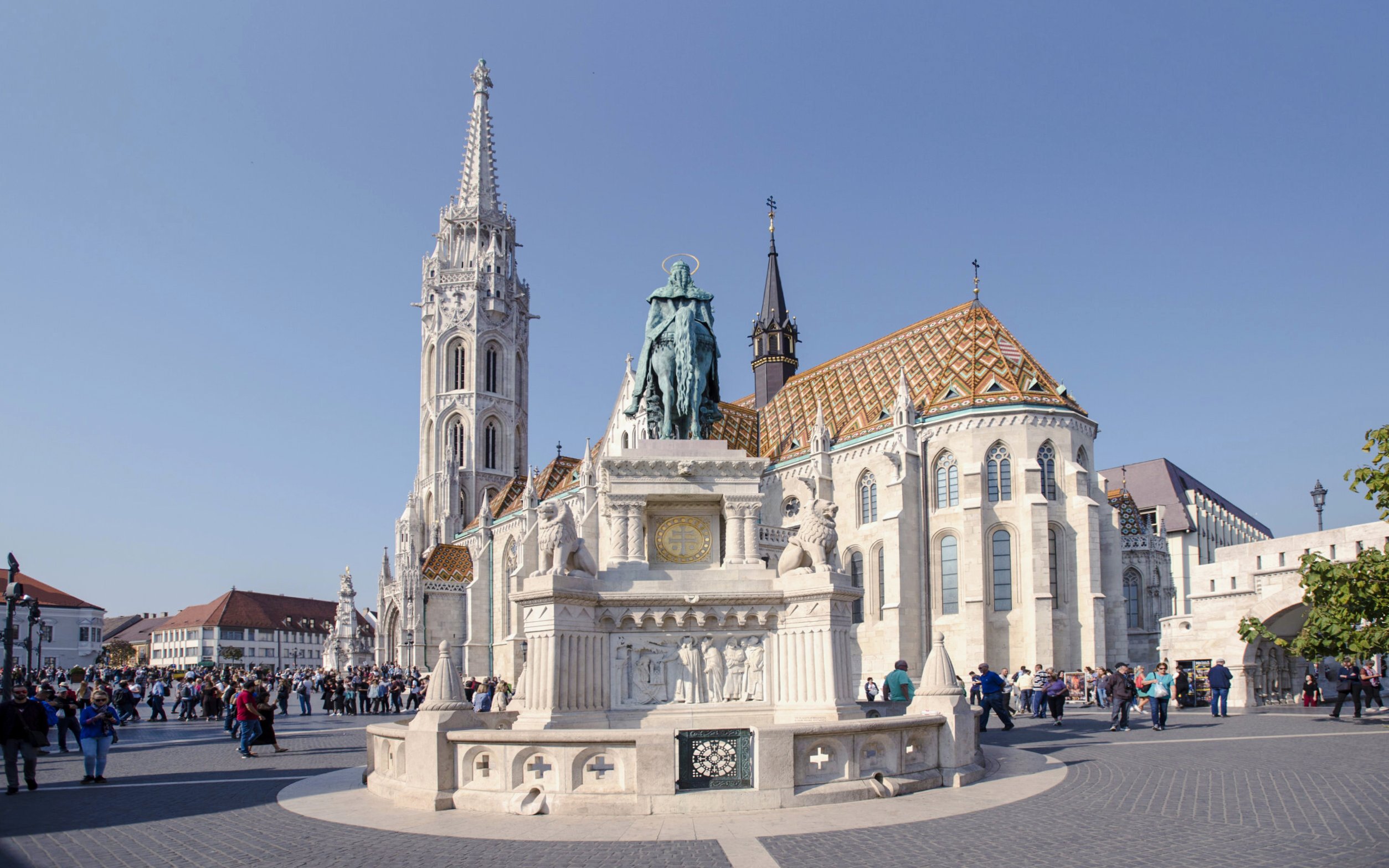 Matthias Church and Holy Trinity Statue in Budapest, Hungary, with tourists exploring the square.