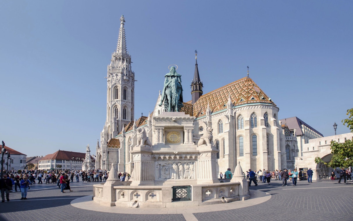Matthias Church and Holy Trinity Statue in Budapest, Hungary, with tourists exploring the square.