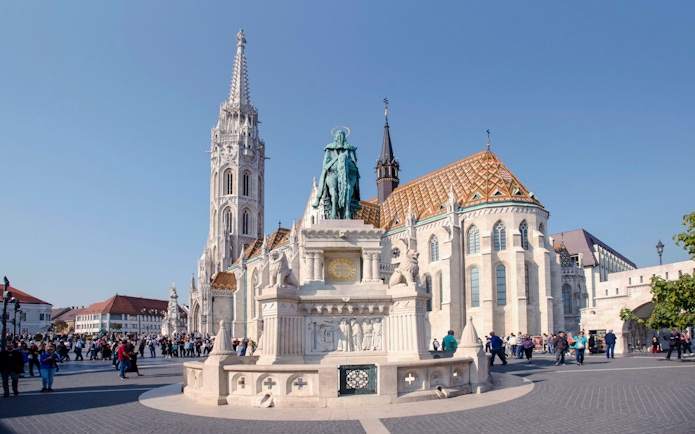 Matthias Church and Holy Trinity Statue in Budapest, Hungary, with tourists exploring the square.