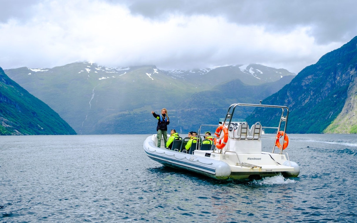 RIB boat with tourists on Geiranger Fjord safari, surrounded by mountains.