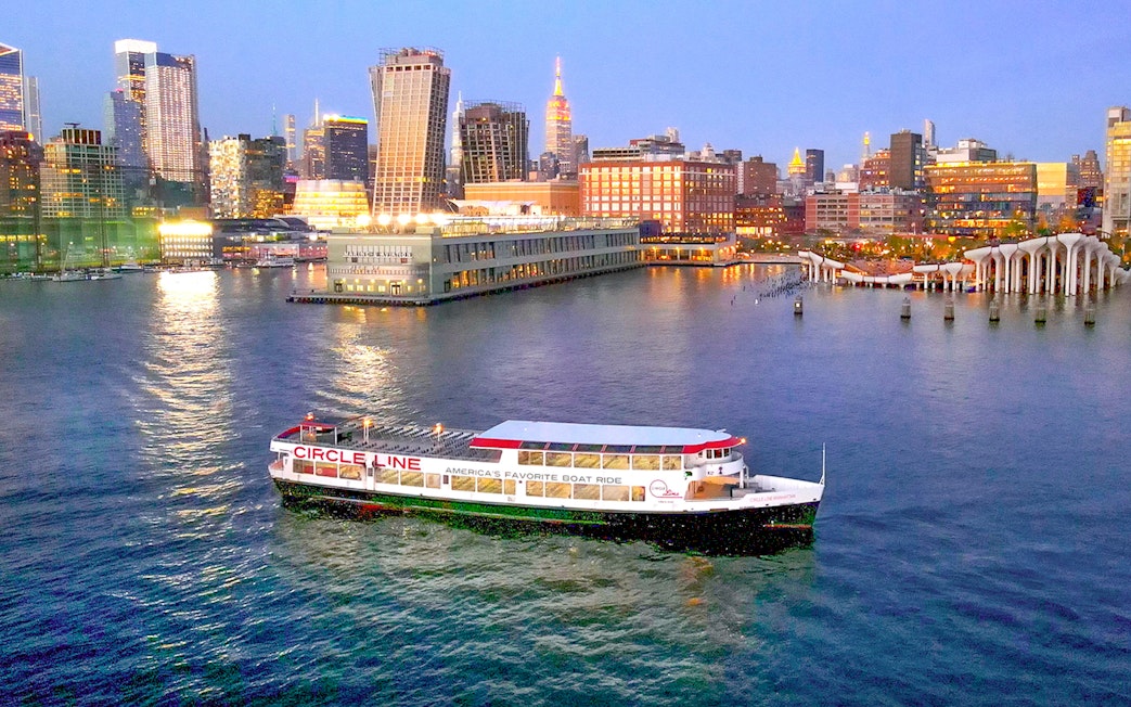 Circle Line cruise boat on Hudson River with New York City skyline at dusk.
