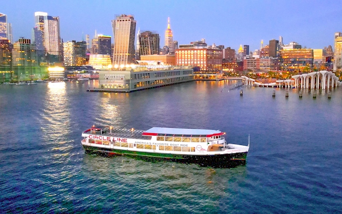 Circle Line cruise boat on Hudson River with New York City skyline at dusk.