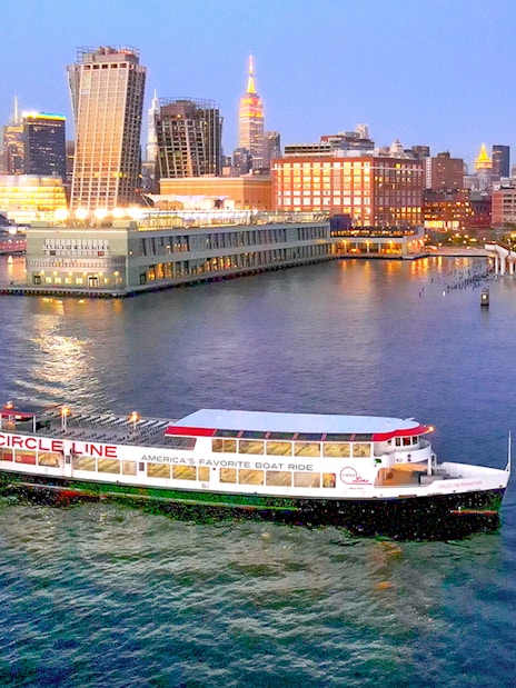 Circle Line cruise boat on Hudson River with New York City skyline at dusk.