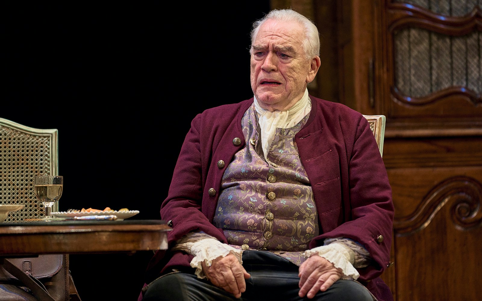 Elderly man in period costume sitting at a table with a drink and food, related to "The Score.