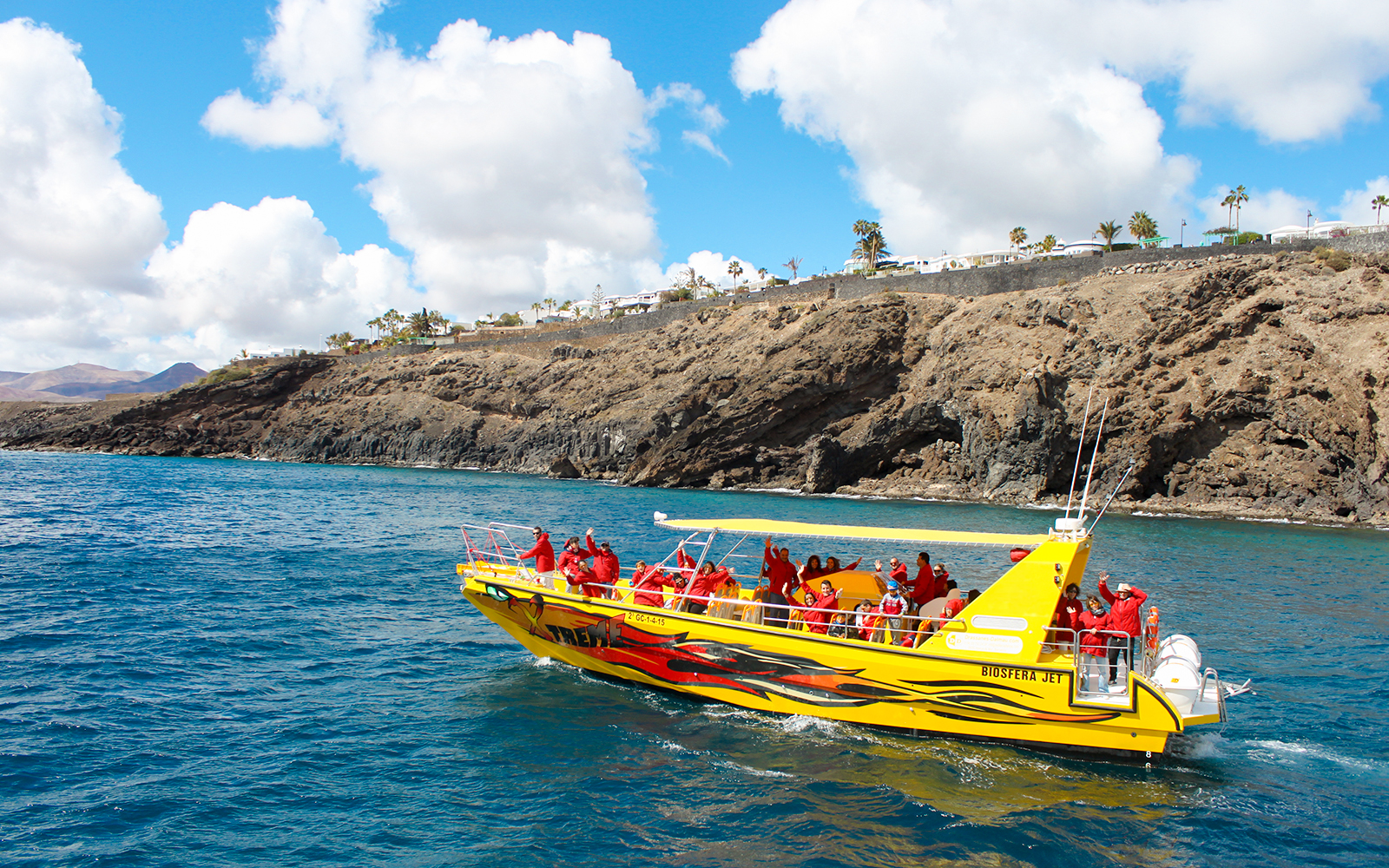 Tourist boat departing port for dolphin watching near rocky coastline.