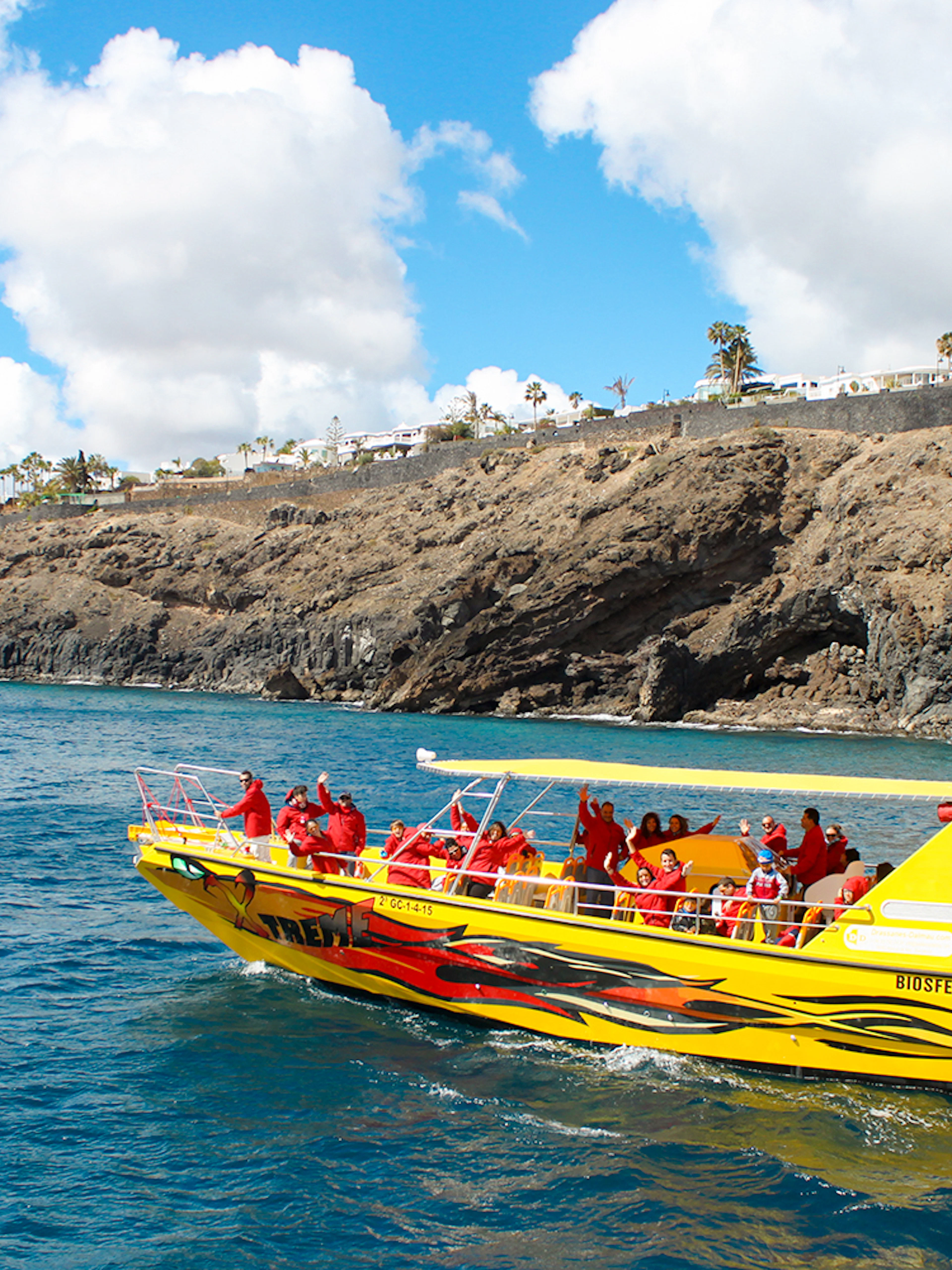 Tourist boat departing port for dolphin watching near rocky coastline.