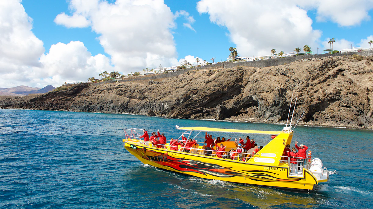 Tourist boat departing port for dolphin watching near rocky coastline.