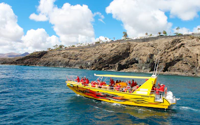 Tourist boat departing port for dolphin watching near rocky coastline.