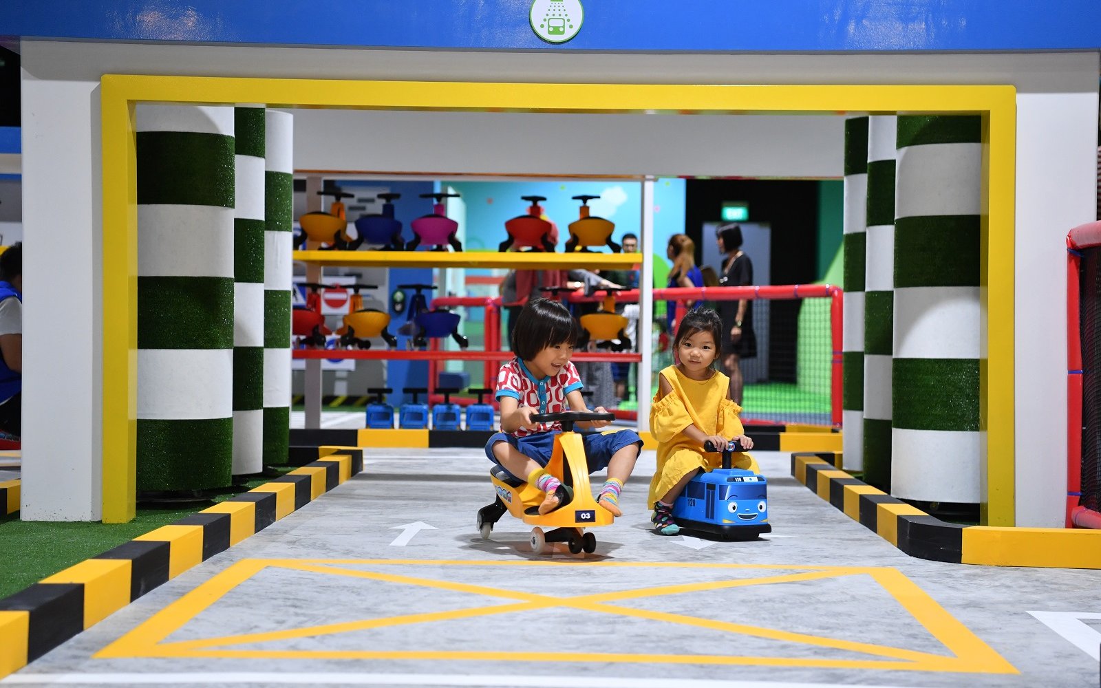 Kids riding tricycles at Tayo Station indoor play area.