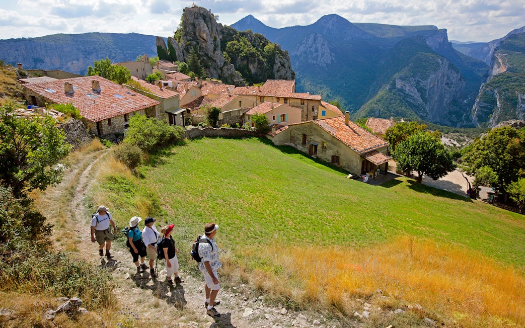 Hikers walking through a village with Gorges du Verdon cliffs in the background.